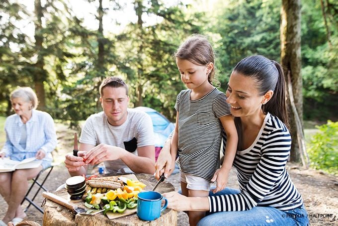 Mama, Papa und Tochter schnibbeln Gemüse im Garten